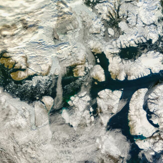 An aerial view shows a partially snow-covered archipelago with dark waterways and swirling clouds.