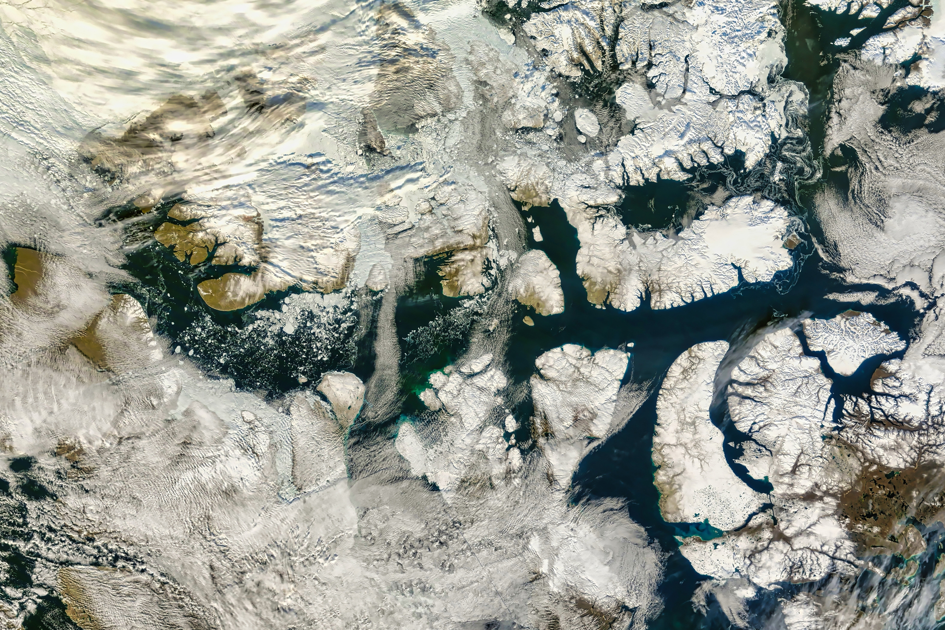 An aerial view shows a partially snow-covered archipelago with dark waterways and swirling clouds.